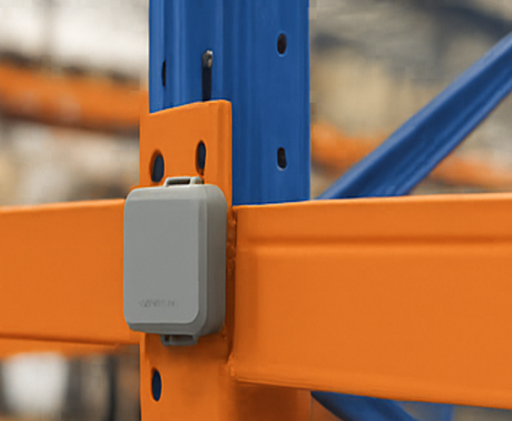 En Square Impact-sensor fastskruvad på stolpen i ett orange och blått pallställ, i höjd med en balk, i en lagergång